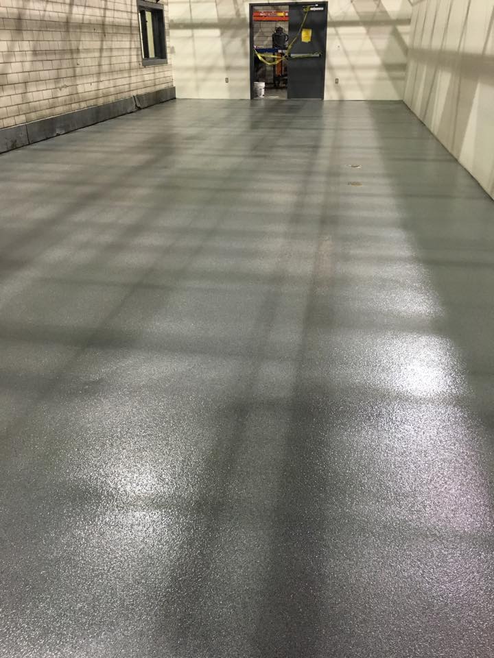 Freshly coated gray epoxy floor in an industrial space, showcasing a sleek, shiny finish. Relevant for illustrating flooring solutions in commercial settings.