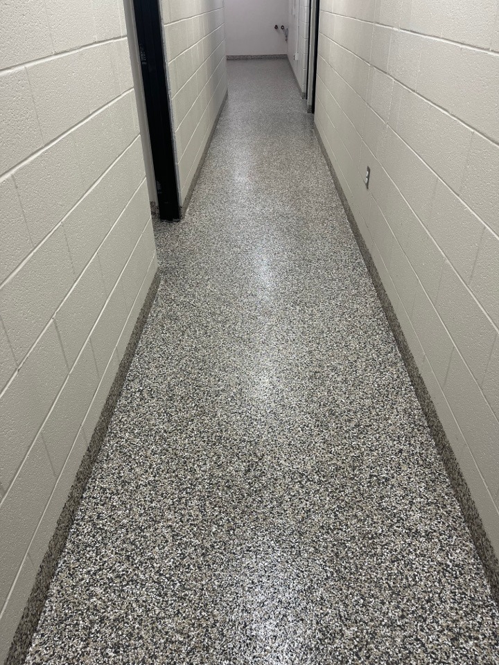 A clean, polished hallway lined with light gray walls and a speckled gray floor. This image showcases the indoor corridor's neat design and maintenance.