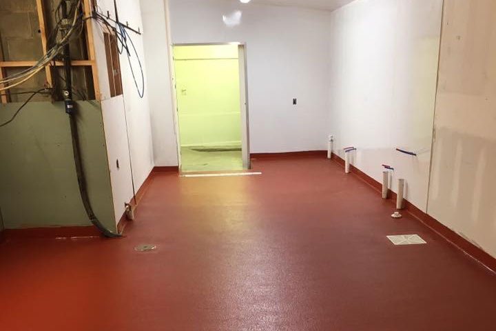 Renovated room with red flooring and unfinished walls. Doorway leads to another space, showcasing progress in construction or remodeling.